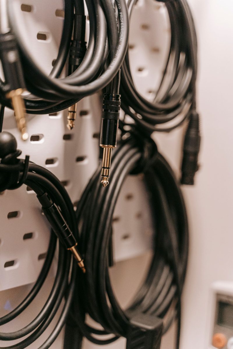 Black audio cables coiled and hung on a pegboard, with quarter-inch plugs and a female XLR connector visible